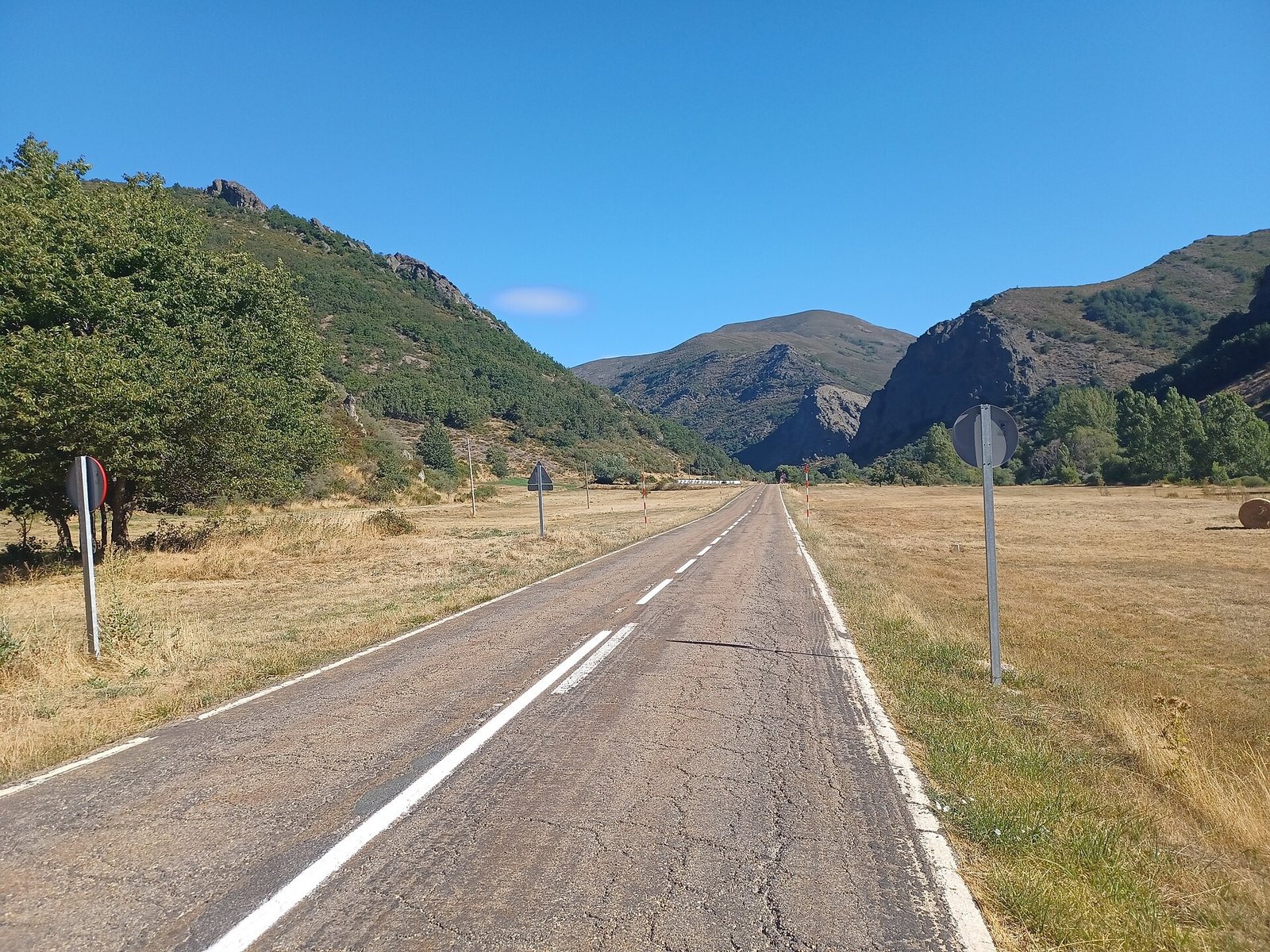 Carretera de doble sentido con línea central discontinua y líneas de borde, vista desde el carril derecho