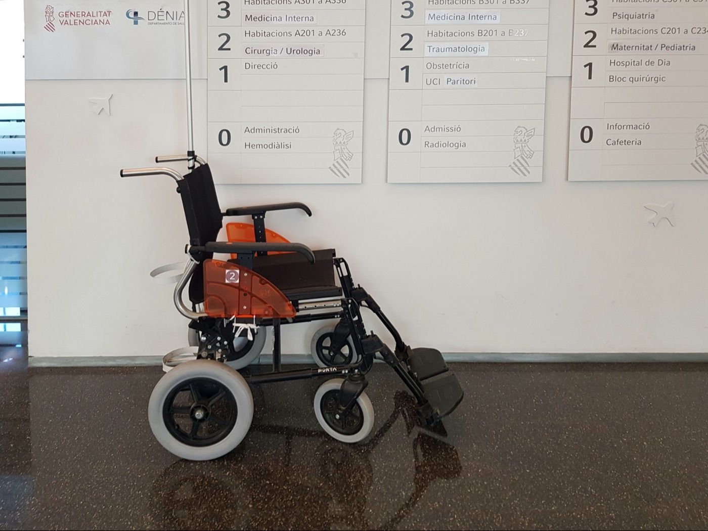 Silla de ruedas manual vacía junto a paneles de orientación en un hospital